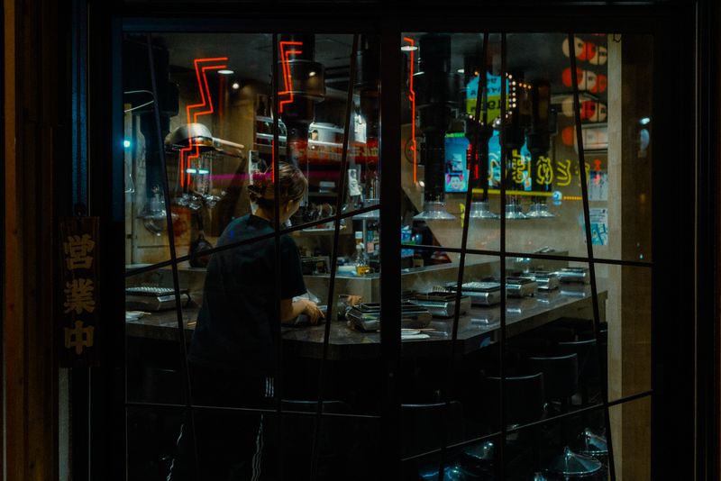 Cameriera di spalle al bancone vista attraverso la vetrata, insegna 営業中 accanto alla porta, Osaka