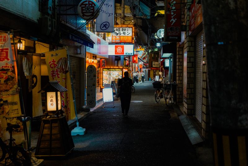 Figura solitaria di spalle in un vicolo di izakaya sotto le insegne del banco dei pegni, Osaka
