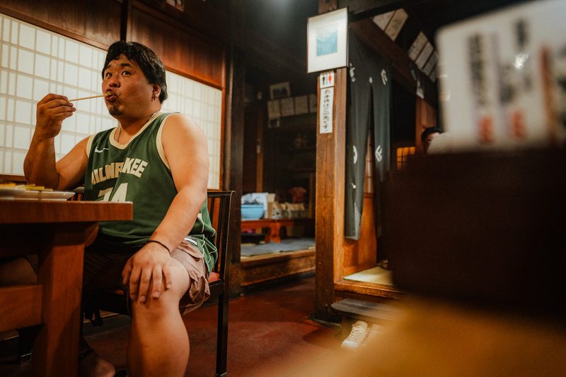 Uomo con canotta da basket mangia in una locanda tradizionale, regione di Hida, Shirakawa-gō