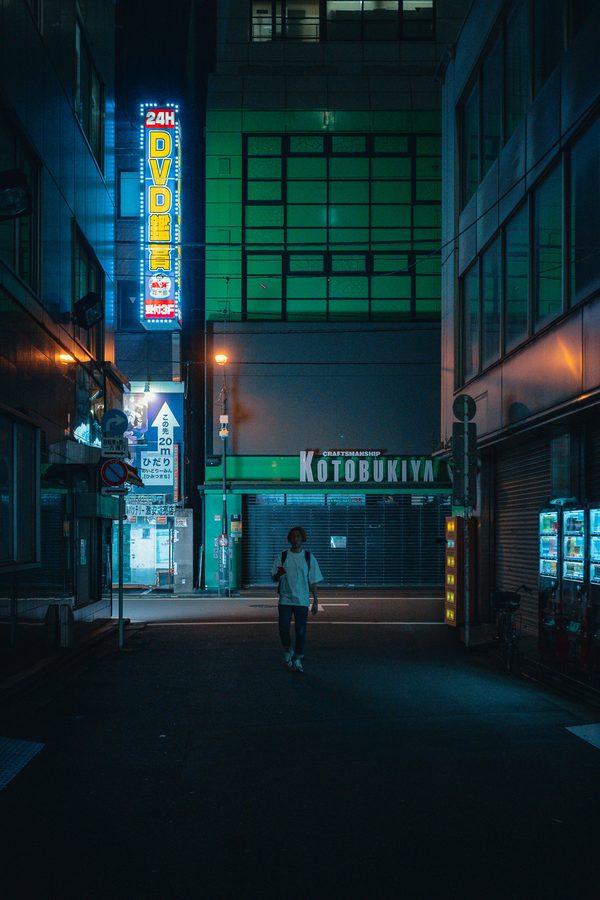 Figura solitaria attraversa una strada quasi buia sotto un’insegna al neon accesa tutta la notte, Akihabara, Tokyo