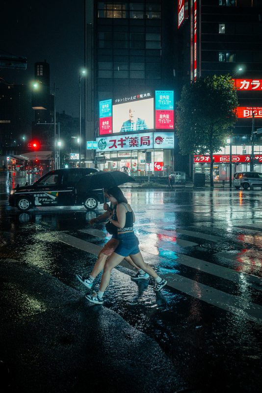 Ragazza con ombrello attraversa le strisce mentre passa un taxi, notte di pioggia, Tokyo