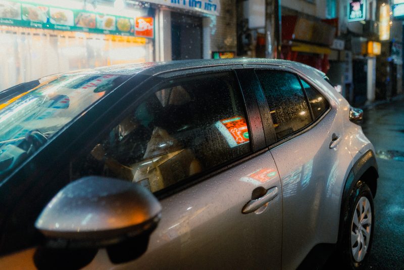Riflessi al neon sulla carrozzeria bagnata di un'auto parcheggiata, notte di pioggia, Tokyo