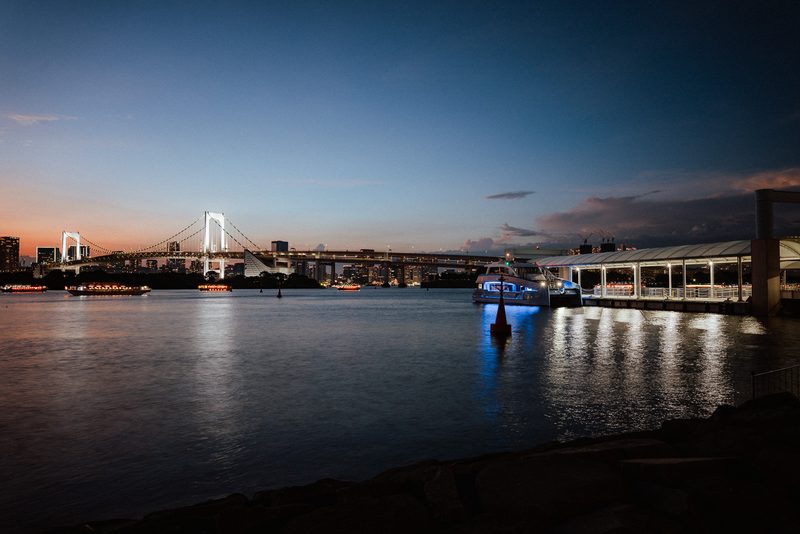 Rainbow Bridge e un molo illuminato nell'ora blu, baia di Tokyo