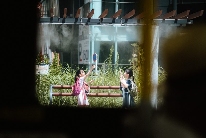 Due bambine giocano con la nebbia di un nebulizzatore urbano, di giorno, Tokyo