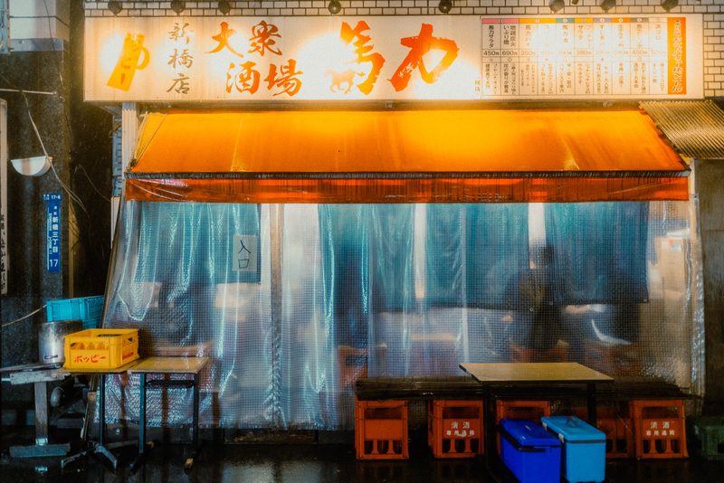 Facciata dell'izakaya Bariki con tenda arancione e teli di plastica sotto la pioggia, Shimbashi, Tokyo