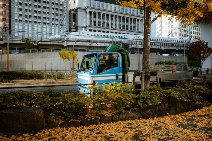 Un camioncino blu parcheggiato accanto a un giardino urbano tra i palazzi di Tokyo
