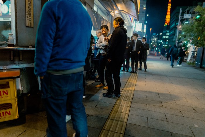 Una fila di persone attende sul marciapiede nella luce della sera, Tokyo
