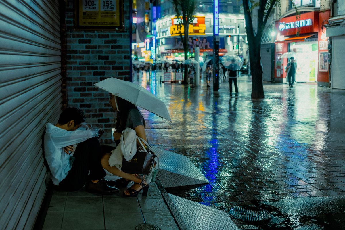 Coppia seduta a terra contro una serranda chiusa mentre piove, Shinjuku, Tokyo
