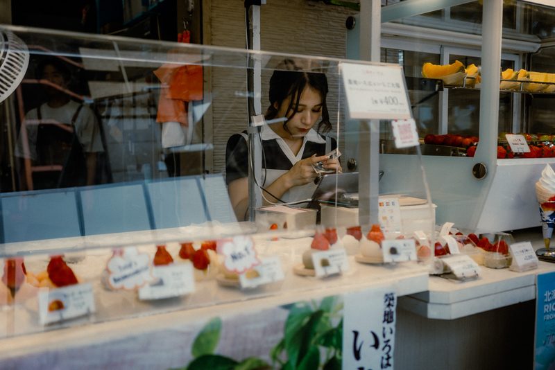 Ragazza conta il denaro dietro il banco dei daifuku alle fragole, mercato di Tsukiji, Tokyo