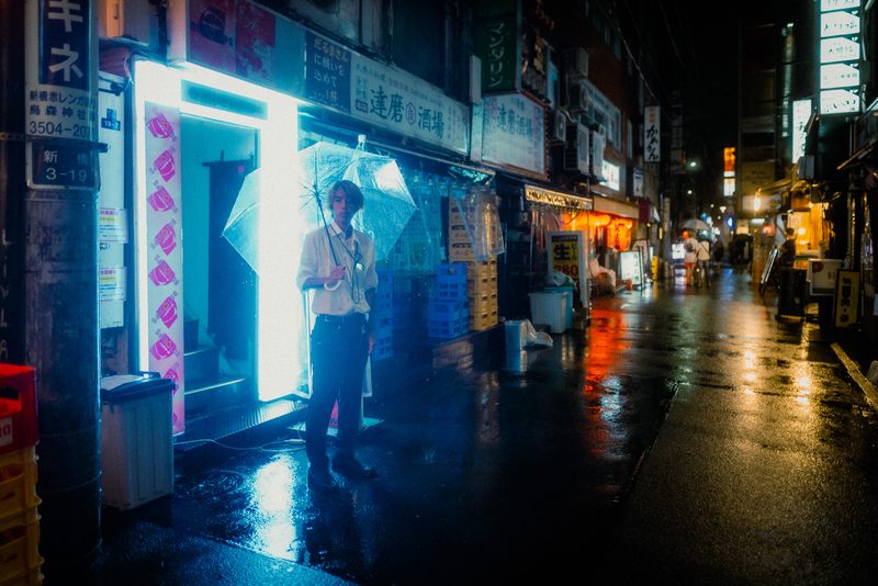 Ragazzo con ombrello trasparente sotto un'insegna al neon bianca davanti al Daruma Sakaba, notte di pioggia, Shimbashi, Tokyo