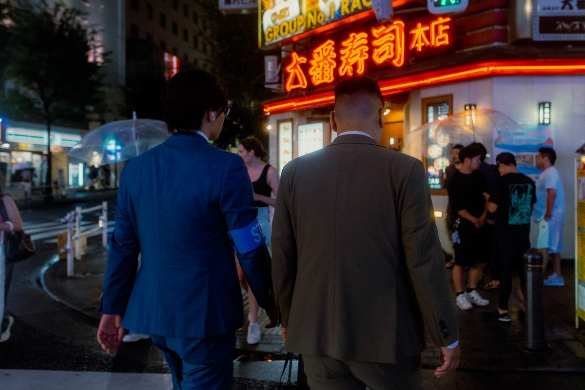 Due uomini in completo di spalle davanti all’insegna al neon di un sushi, Shinjuku, Tokyo
