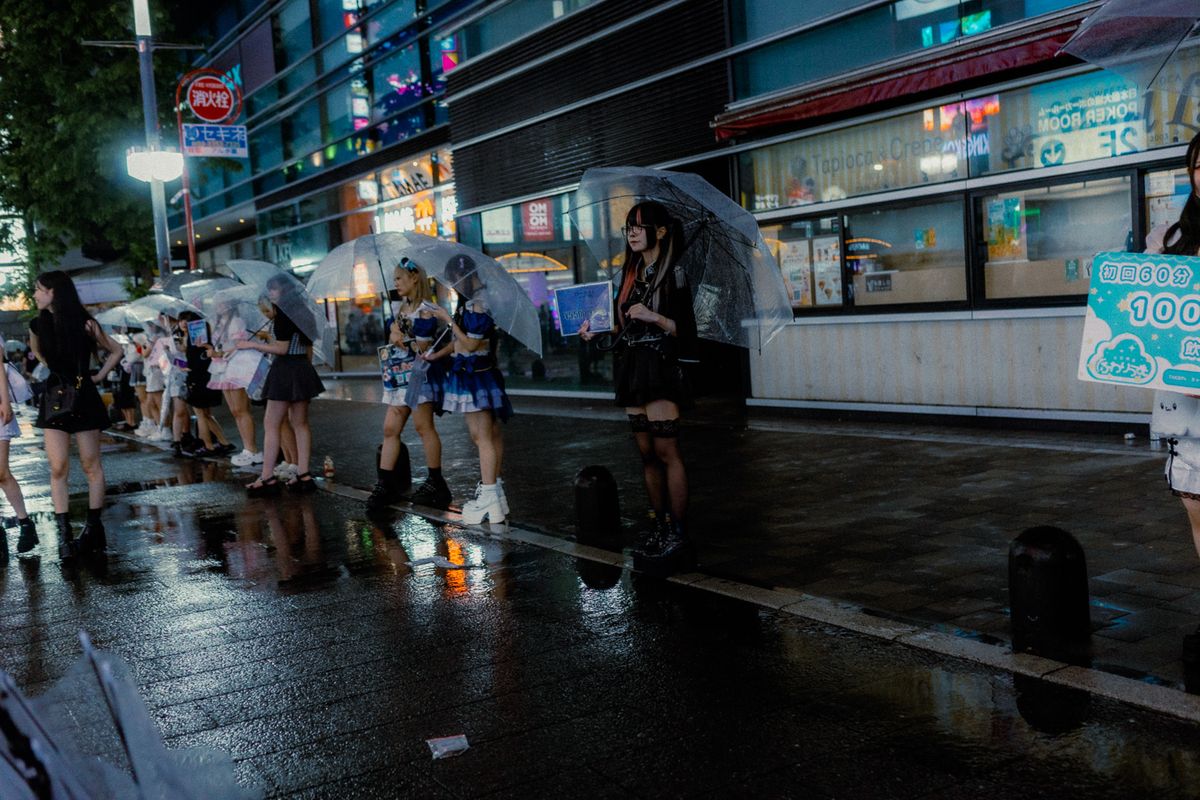 Ragazze in fila sul marciapiede con ombrelli trasparenti e cartelli pubblicitari, Tokyo