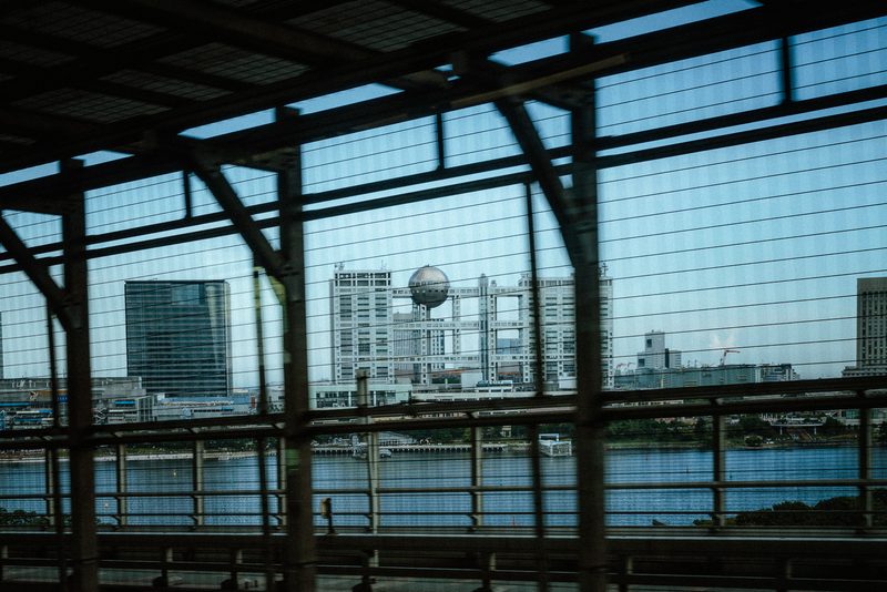 Il palazzo della Fuji TV con la sfera visto attraverso la struttura di una stazione, baia di Tokyo