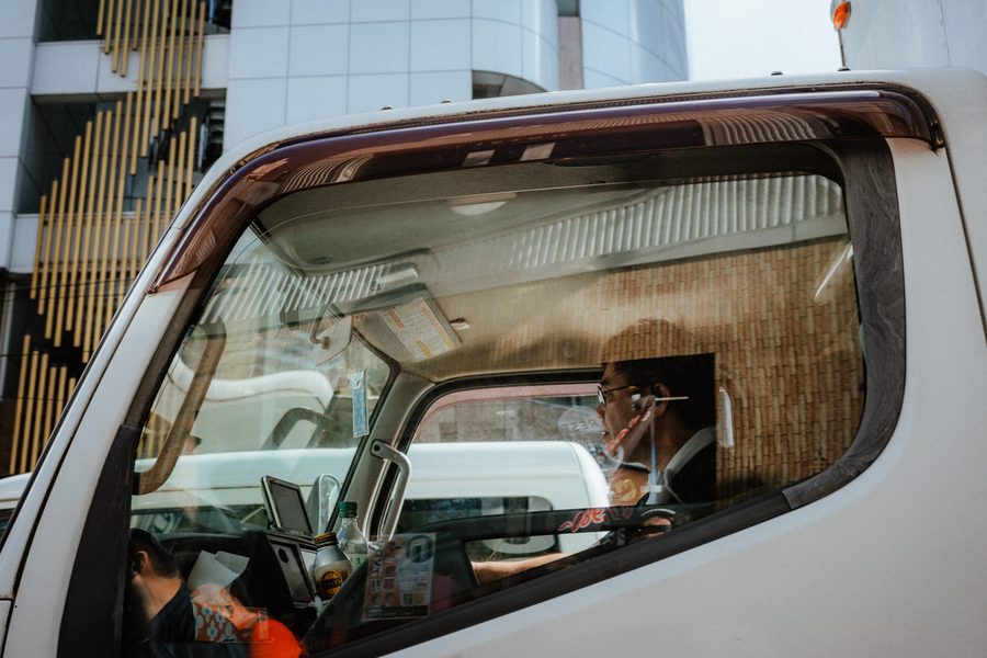Autista con occhiali e auricolare al volante di un furgone bianco, visto dal finestrino laterale, Tokyo