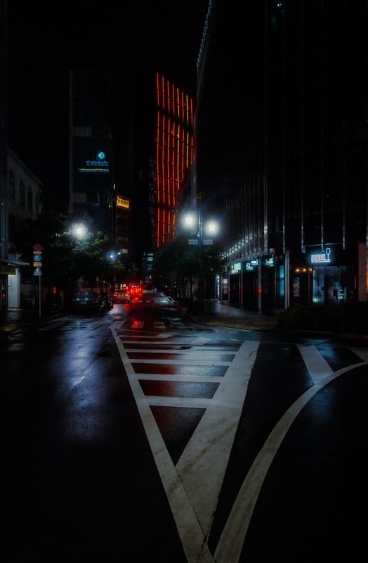 Incrocio deserto bagnato dalla pioggia con un grattacielo dalle luci rosse, di notte, Tokyo