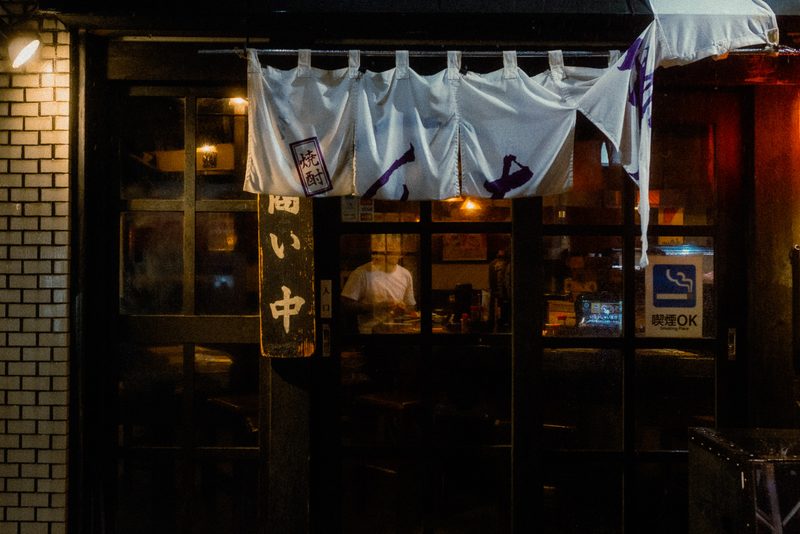 Ingresso di un izakaya con noren bianco e insegna aperto, di notte sotto la pioggia, Tokyo