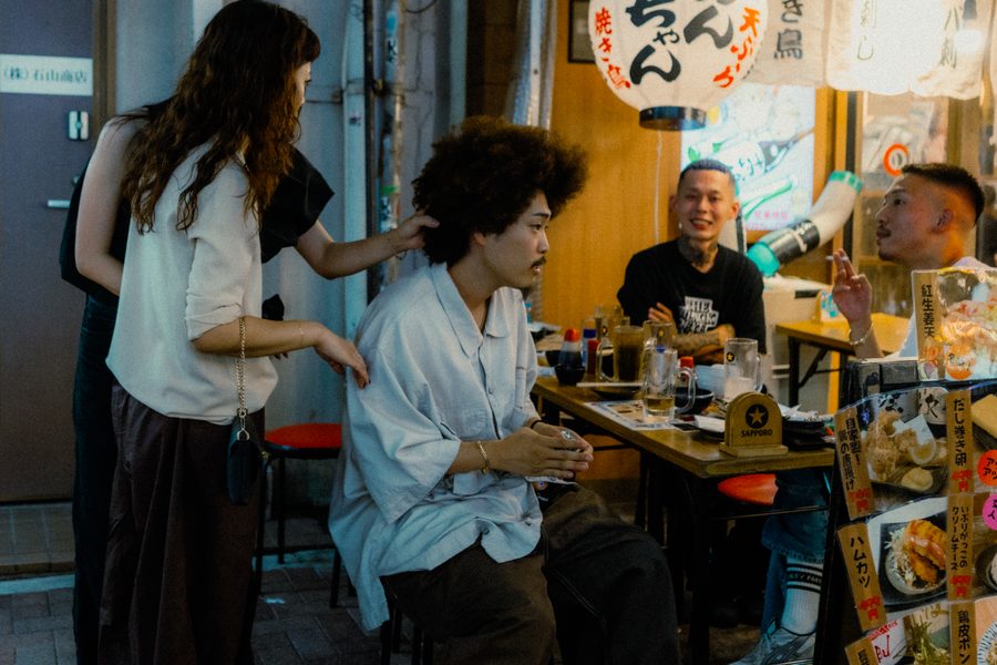 Gruppo di amici a un tavolo all’aperto di un izakaya sotto la lanterna di carta, di sera, Tokyo