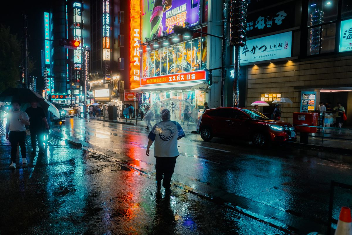 Uomo con ombrello trasparente attraversa la strada bagnata davanti alle insegne, Kabukichō, Tokyo