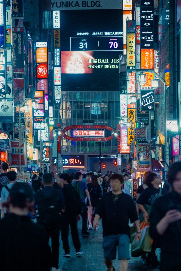La folla avanza verso l’arco luminoso di Kabukichō Ichiban-gai tra le insegne verticali, notte, Tokyo