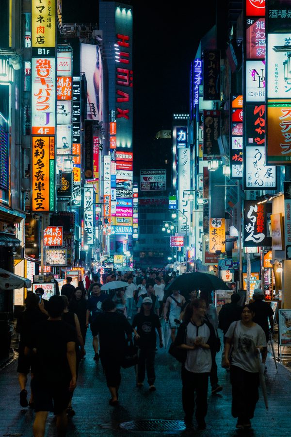 Strada di Kabukichō gremita di insegne al neon e passanti con gli ombrelli sotto la pioggia, Tokyo