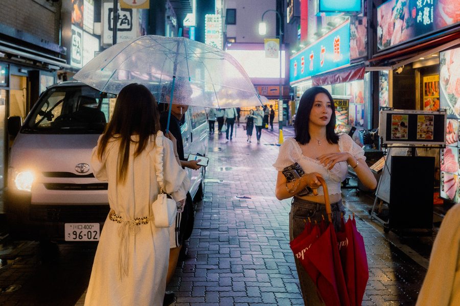 Due donne in una via commerciale sotto la pioggia, un ombrello trasparente e uno rosso chiuso, insegne al neon, Kabukichō, Tokyo