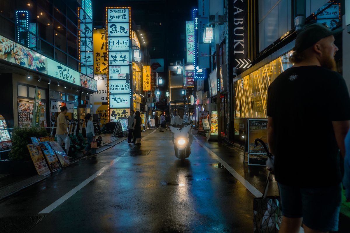 Uno scooter risale la strada bagnata tra le insegne delle izakaya, Kabukichō, Tokyo