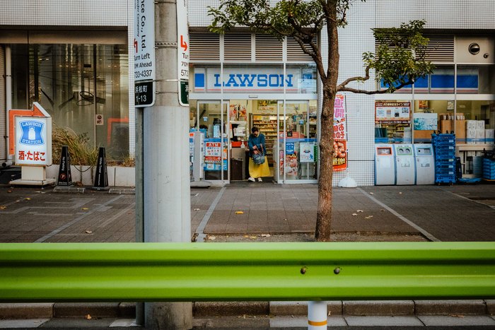 Un konbini Lawson visto oltre la barriera verde di una stazione di Tokyo