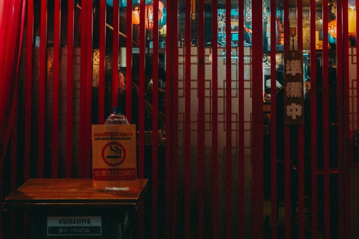 Un tavolino vuoto dietro i listelli rossi di un locale di Tokyo