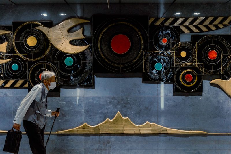 Anziano con bastone cammina davanti al murale astratto a cerchi di una stazione della metro, Tokyo