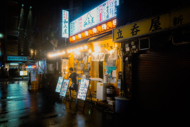 Uomo davanti al menu dell'izakaya Nagomiya con lanterne di carta, notte di pioggia, Shimbashi, Tokyo