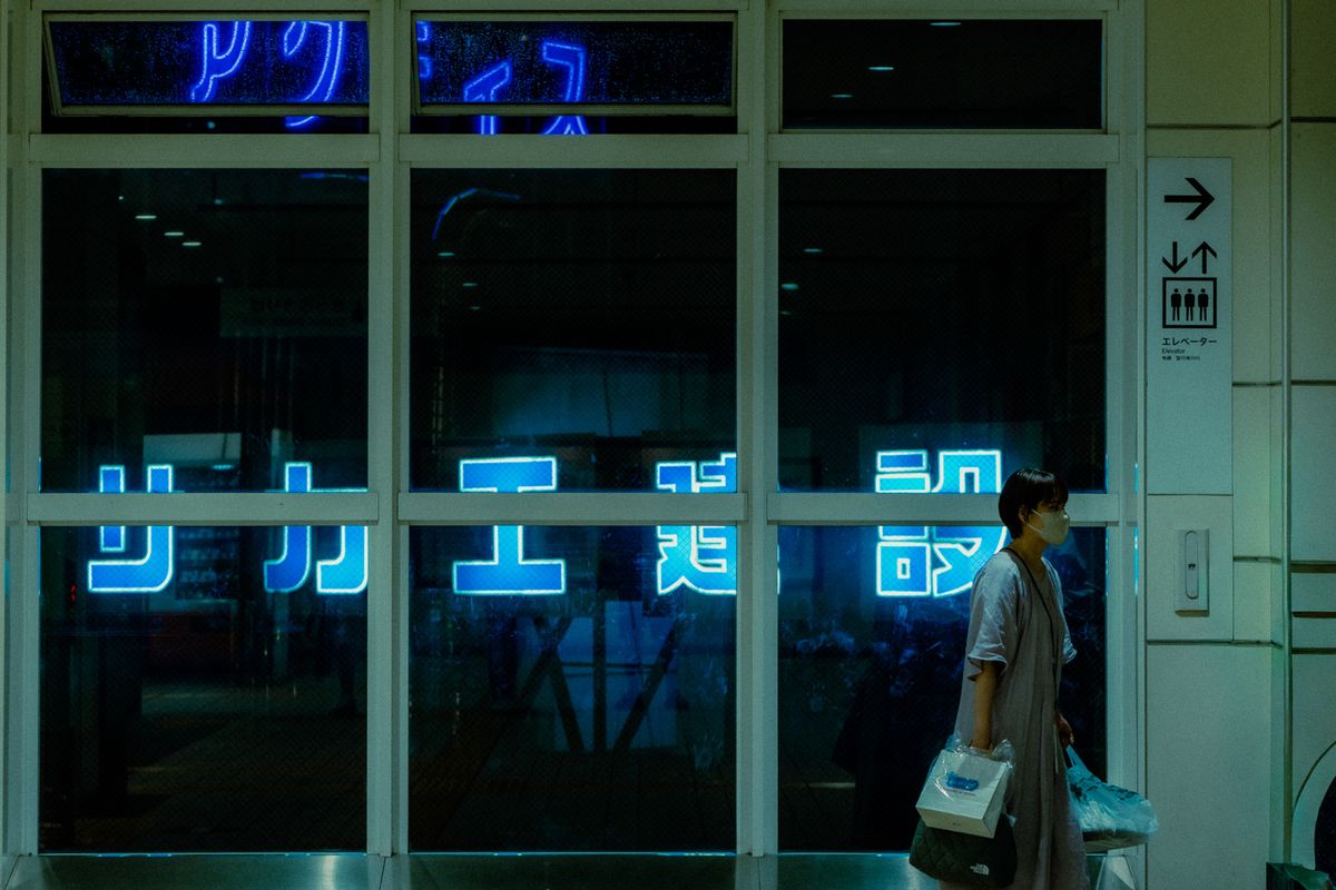 Donna cammina davanti a una vetrata con grandi neon blu, Tokyo