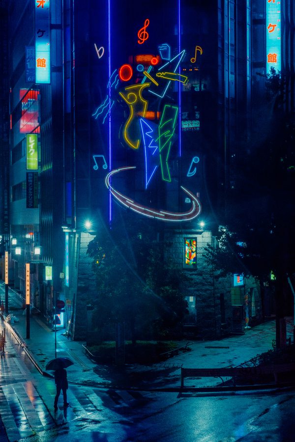 Grande insegna al neon con la figura di un musicista sopra un passante con l’ombrello, Nishi-Shinjuku sotto la pioggia, Tokyo