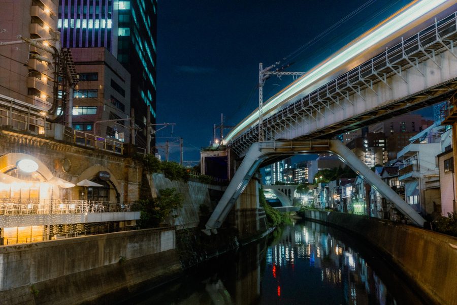 Treno mosso sul ponte ferroviario sopra il canale, con i riflessi delle luci sull’acqua, Ochanomizu, Tokyo