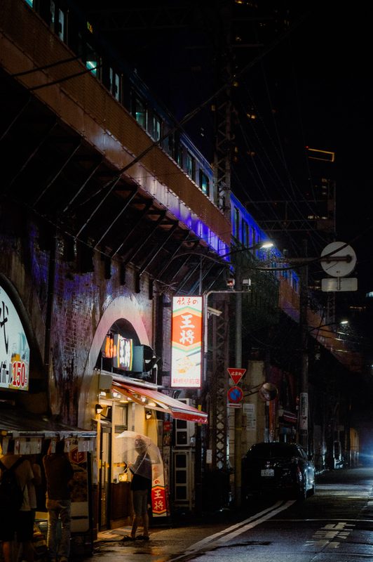 Insegna del ristorante di gyoza Ohsho sotto la ferrovia con un treno che passa, notte di pioggia, Shimbashi, Tokyo