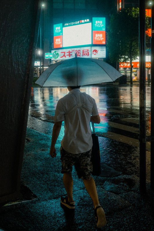 Uomo di spalle con ombrello davanti alle insegne al neon di Shimbashi, notte di pioggia, Tokyo