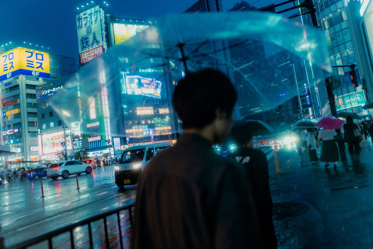 Uomo di spalle con ombrello trasparente a un incrocio bagnato dalla pioggia, Shinjuku, Tokyo