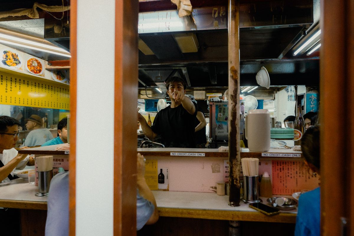 Il cuoco dietro il banco indica l’obiettivo in una tavola calda di Omoide Yokochō, Tokyo