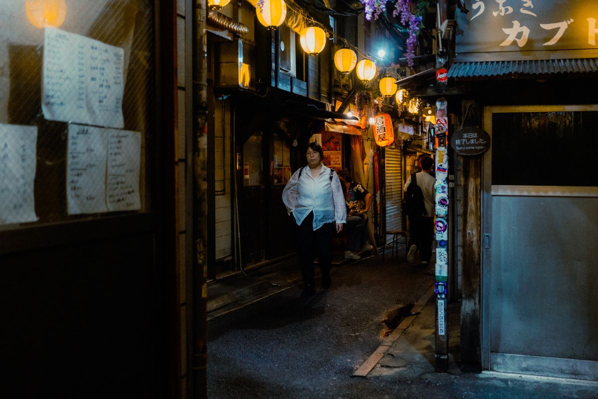 Donna in camicia bianca cammina nel vicolo delle lanterne di Omoide Yokochō, Shinjuku, Tokyo
