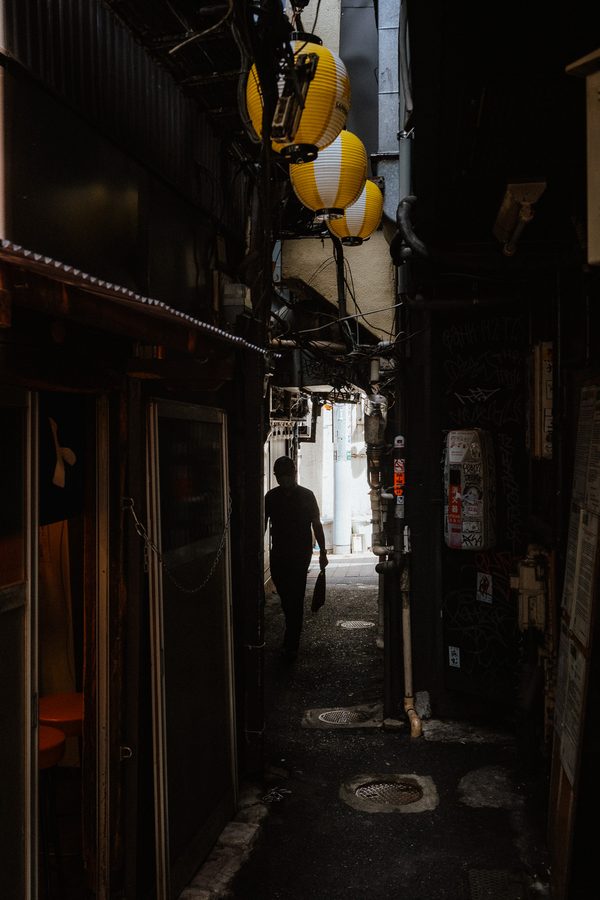 Silhouette di un uomo in fondo a un vicolo stretto sotto le lanterne di carta gialle, Omoide Yokochō, Tokyo