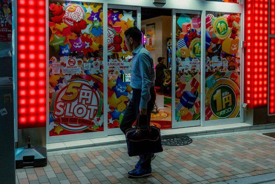 Uomo con una borsa passa davanti alle vetrine colorate di una sala pachinko tra i led rossi, Tokyo