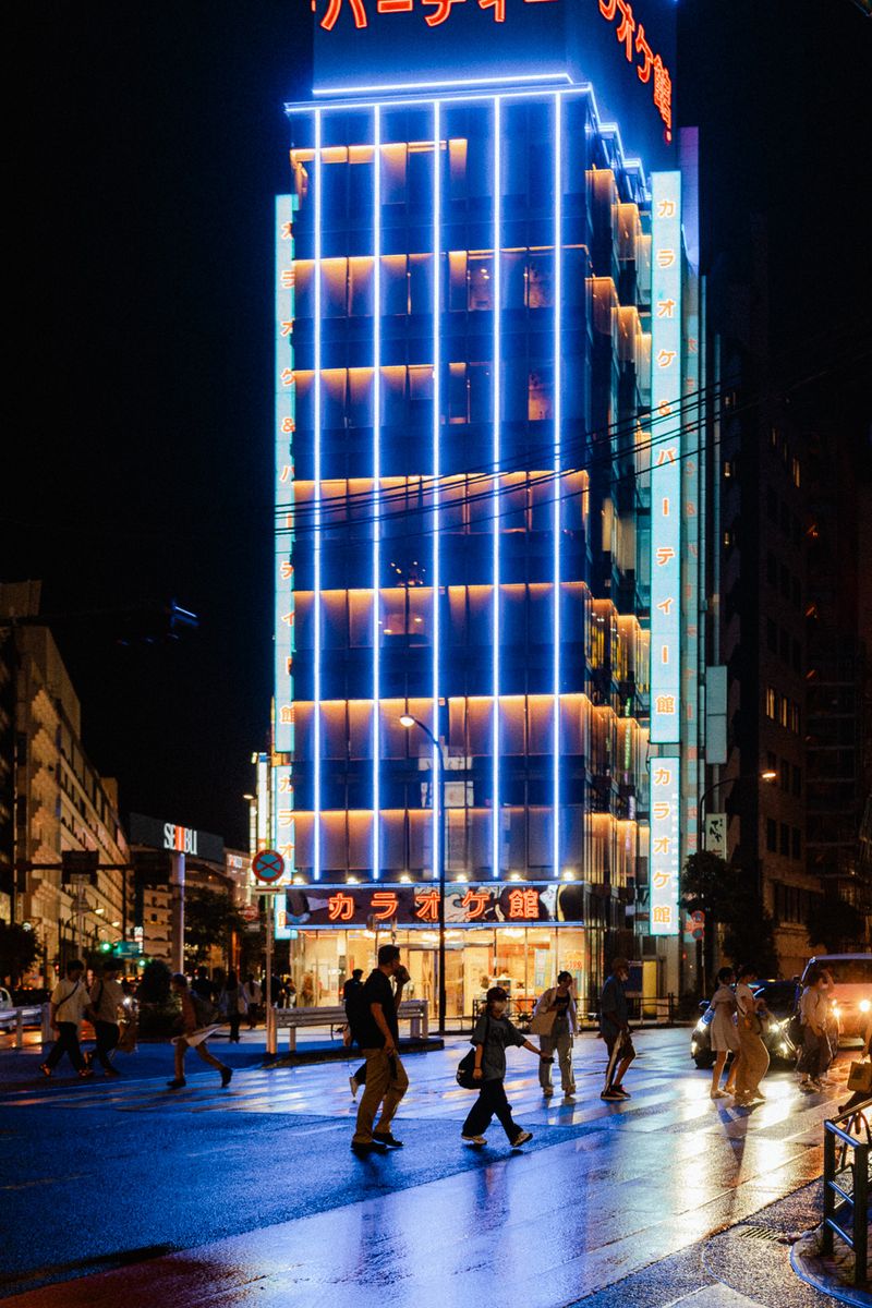 Palazzo di un karaoke illuminato di blu sopra un attraversamento bagnato, Tokyo