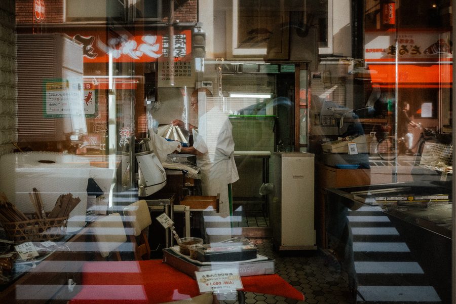 Interno di una pescheria visto attraverso la vetrina, con i riflessi della strada sovrapposti, Tokyo