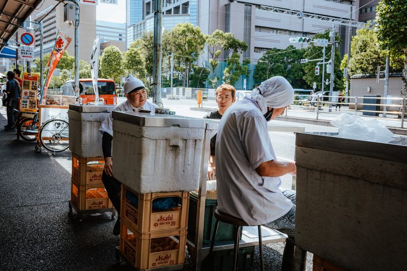 Pescivendoli in pausa attorno ai contenitori e alle casse Asahi, mercato di Tsukiji, Tokyo