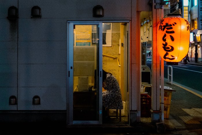Una porta illuminata accanto a una lanterna arancione in un vicolo di Tokyo