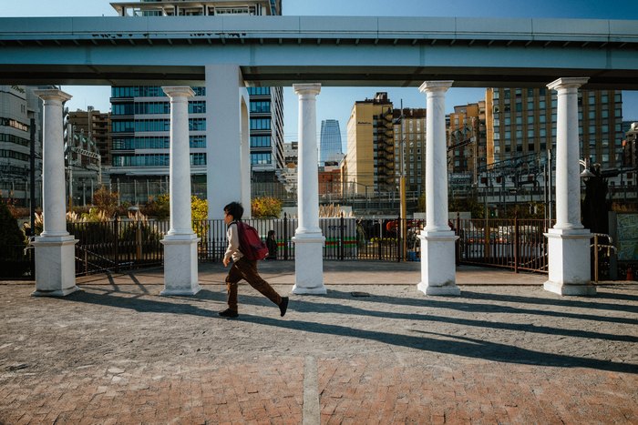 Due persone attraversano un porticato bianco tra gli edifici di Tokyo