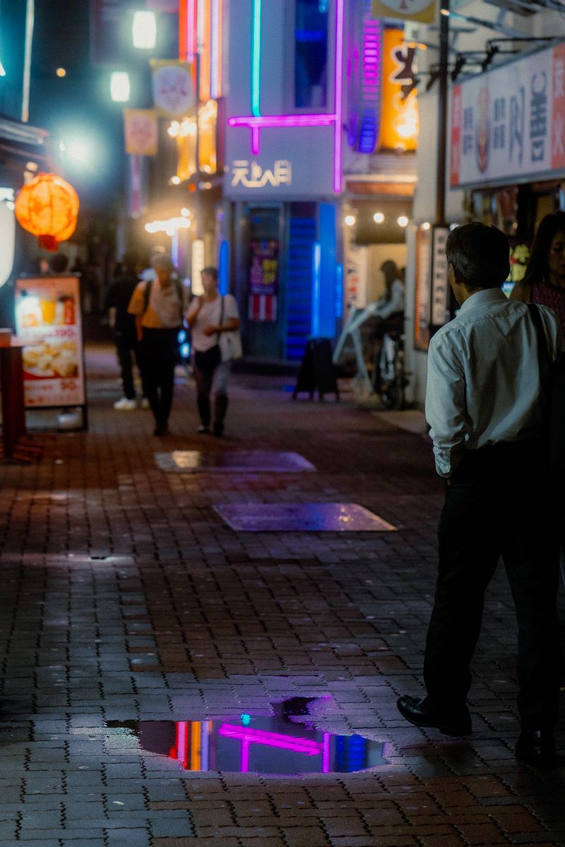 Un neon viola riflesso in una pozzanghera sul selciato, Shinjuku, Tokyo