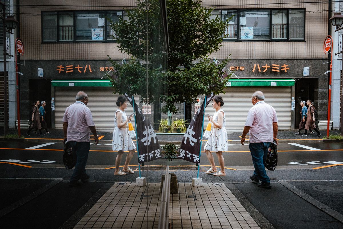Passanti raddoppiati dal riflesso di una vetrata su una strada di quartiere, Tokyo