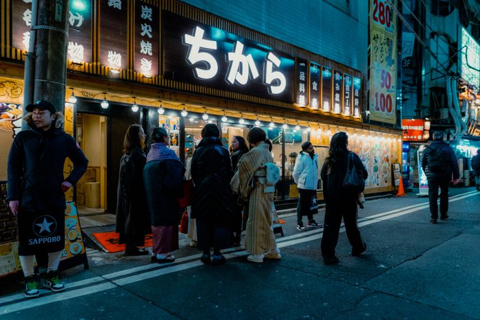 Avventori in fila davanti a un ristorante illuminato nella notte di Tokyo