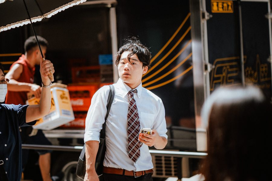 Giovane in camicia bianca e cravatta si volta per strada davanti a un camion in scarico, Tokyo