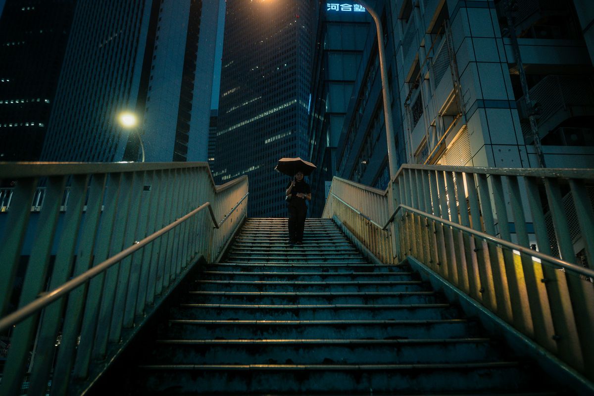 Donna con ombrello scende una scalinata tra i grattacieli, Shinjuku, Tokyo
